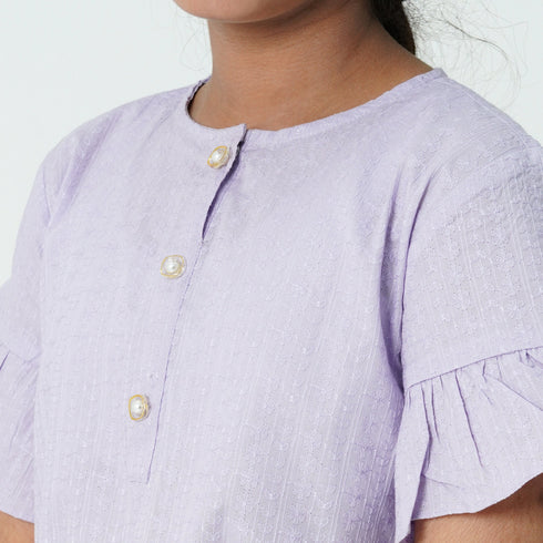 Close-up of a person wearing a light lilac dress with button details on a white background